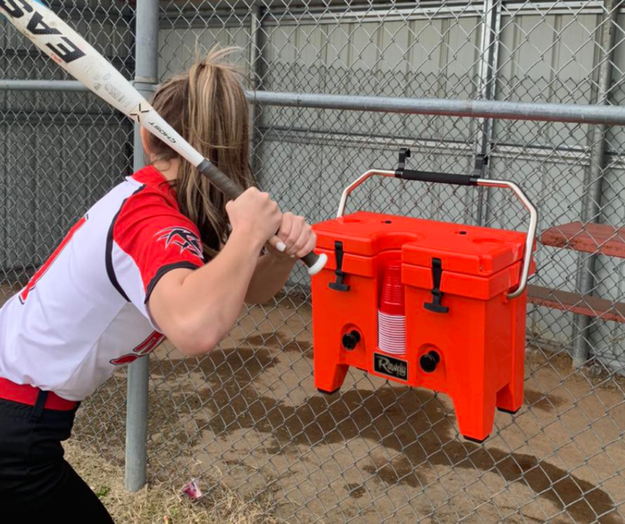 red rowdy cooler hanging on a dugout fence with girl holding a softball bat